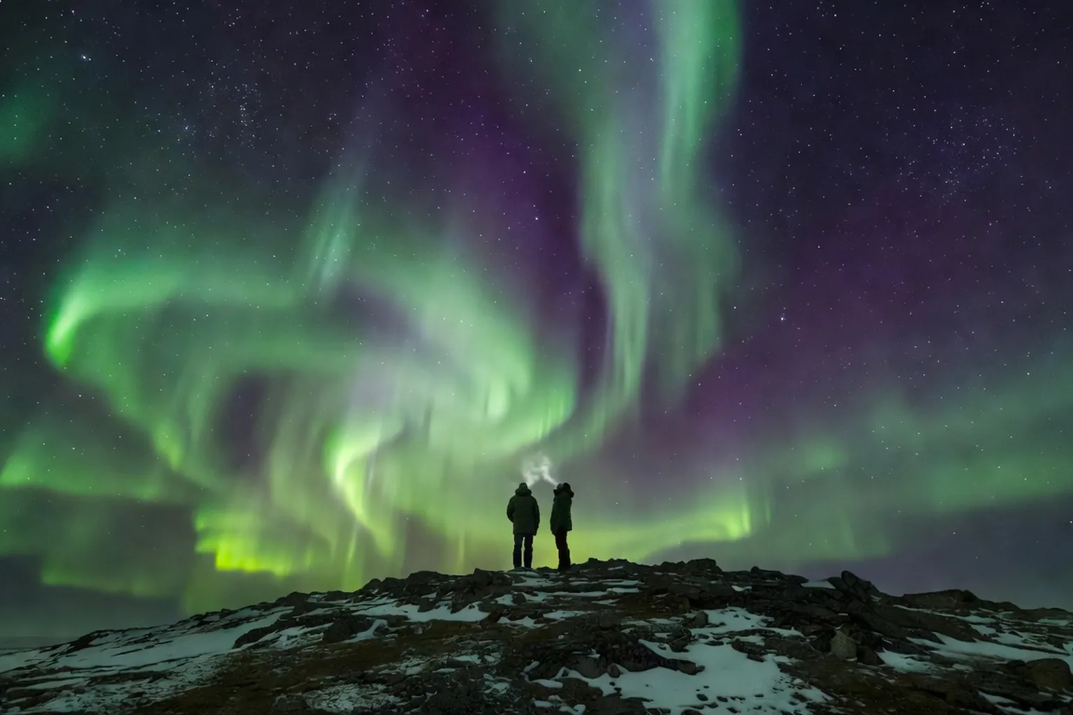 Observateurs sous une aurore boreale verte en montagne enneigee