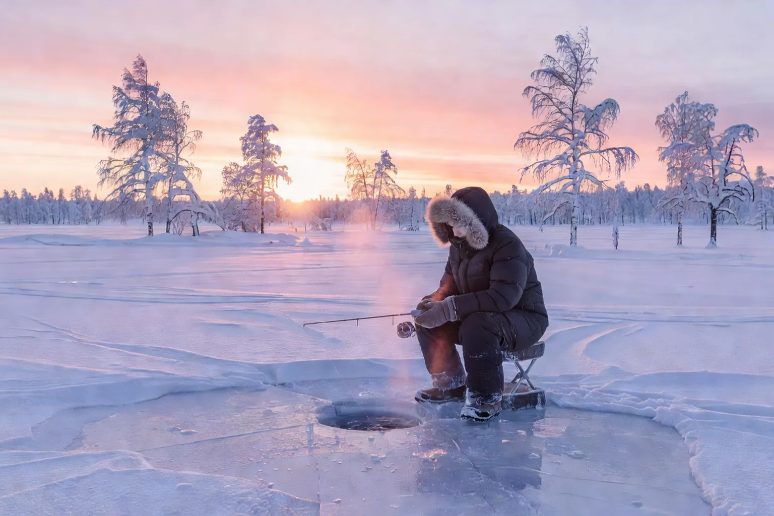 Pêche sur glace sur un lac gelé de Laponie finlandaise au lever du soleil