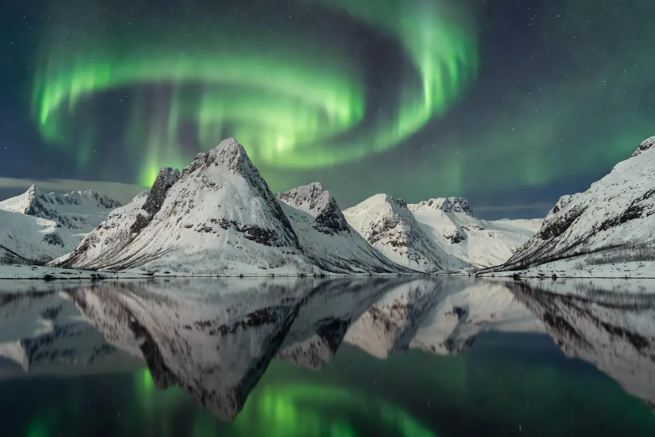 Alpes du Lyngen sous aurores boréales vertes avec reflets dans le fjord en hiver